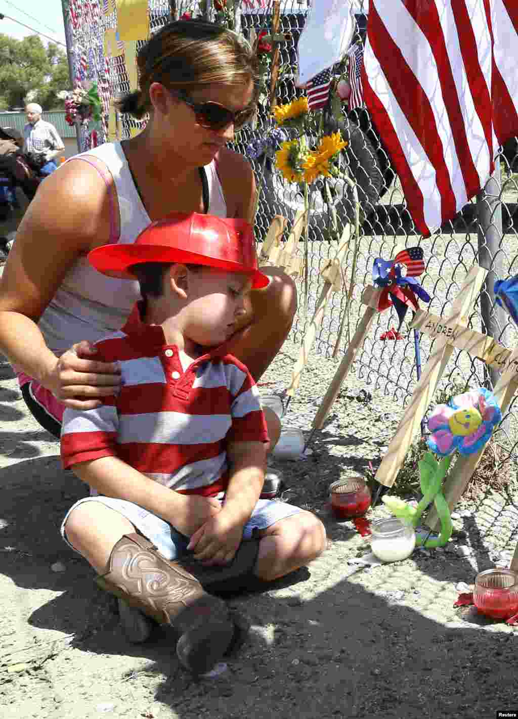 Casen Beyea, 3, wearing a toy fireman helmet looks at the cross for Andrew Ashcrast with his mother Christine at a memorial in Prescott, Arizona, July 2, 2013. 