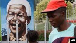 A child looks through a fence at a portrait of former president Nelson Mandela in a Park in Soweto, South Africa, Mar. 28, 2013.