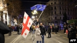 Anti-government protesters wave a Georgian and European Union flag during a demonstration against the Georgian government's postponement of European Union accession talks until 2028, outside the Parliament in Tbilisi, Dec. 12, 2024.