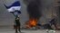 A masked protester waves a Nicaraguan national flag in front of a burning barricade, as protesters clashed with riot police in the Monimbo district of Masaya, Nicaragua, May 12, 2018.