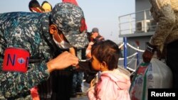 A Bangladesh navy personnel helps a child to wear a mask due to ongoing coronavirus disease (COVID-19) before getting on board a ship to move to Bhasan Char island in Chattogram, Bangladesh, Dec. 29, 2020.