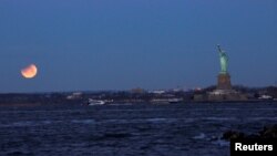 Sebuah “Bulan Darah Biru Super” terjadi dalam gerhana bulan sebagian yang tampak dekat Patung Liberty seperti tampak dari Brooklyn, New York, AS, 31 Januari 2018 (foto: Reuters/Eduardo Munoz)