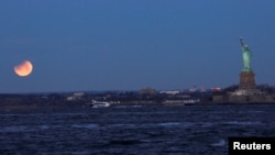 A "Super Blue Blood Moon" sets during a partial lunar eclipse next to the Statue of Liberty as it is seen from Brooklyn, in New York, Jan. 31, 2018. 