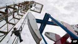 FILE - A worker hangs from an oil derrick outside Williston, North Dakota, where oil is taken from the Bakken shale formation, July 26, 2011.