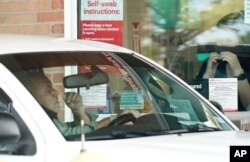 Pharmacy workers give instruction on how to administer a COVID-19 nasal swab self-exam at a drive-up CVS pharmacy in Dallas, Sept. 18, 2020.