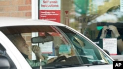 Pharmacy workers give instruction on how to administer a COVID-19 nasal swab self-exam at a drive-up CVS pharmacy in Dallas, Sept. 18, 2020. 