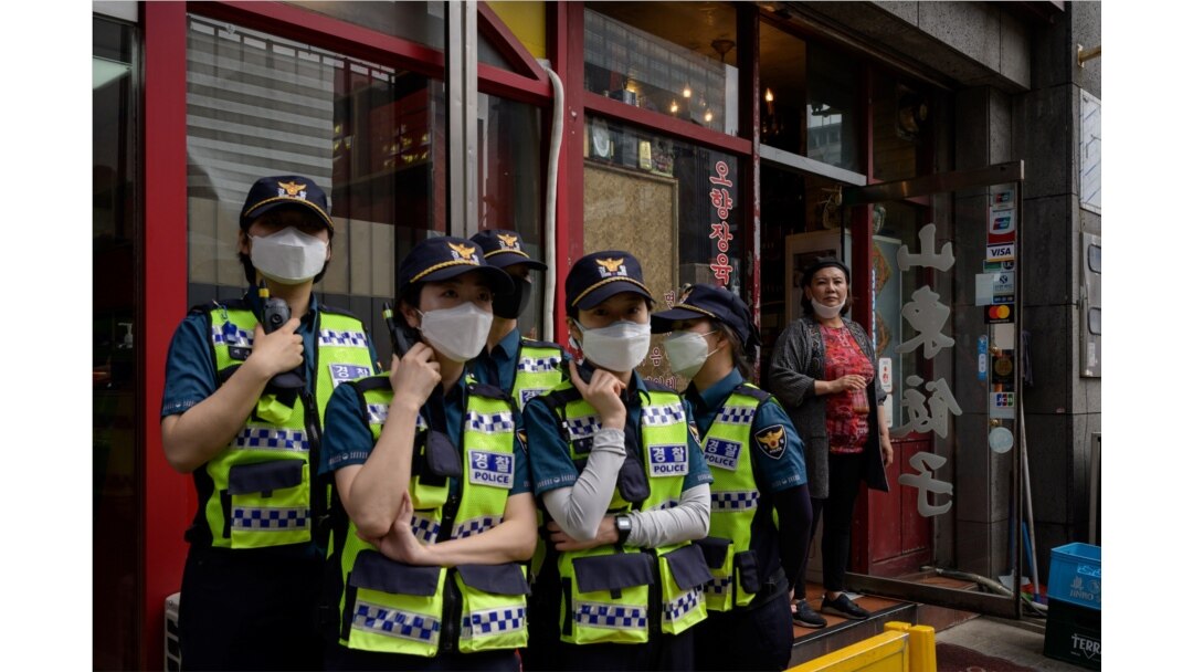 FILE - A woman stands at the door of a Chinese restaurant near China's embassy in Seoul as police officers monitor a group of pro-democracy activists holding a Tiananmen commemoration event, on June 4, 2020.