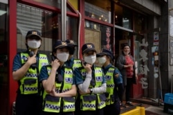 FILE - A woman stands at the door of a Chinese restaurant near China's embassy in Seoul as police officers monitor a group of pro-democracy activists holding a Tiananmen commemoration event, on June 4, 2020.