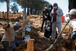 FILE - Relatives of Munevver Kaya, who died of COVID-19, wearing face masks for protection against the coronavirus, offer their prayers during a funeral at a special section of Baklaci cemetery in Istanbul dedicated to COVID victims, May 11, 2020.