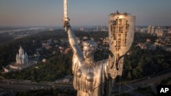 Trabajadores instalan el escudo de armas de Ucrania en el escudo en la mano de la estatura más alta del país, el Monumento a la Patria, luego de que se retirara el escudo de armas soviético, en Kiev, Ucrania, el domingo 6 de agosto de 2023.