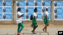 School girls walk past election posters of Togo's incumbent President Faure Gnassingbe, candidate of Union for the Republic, in Lome, Togo, Feb. 21, 2020.