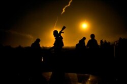 FILE - Syrian Democratic Forces fighters watch illumination rounds light up Baghuz, Syria, as the last pocket of Islamic State militants is attacked, March 12, 2019.