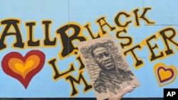 A demonstrator carries an image of George Floyd in front of a boarded up business decorated with a mural reading "All Black Lives Matter," on Hollywood Boulevard, during a march organized by black members of the LGBTQ community in the Hollywood…