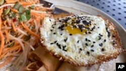 A vegan chorizo egg roll and a meat chorizo egg roll topped with a fried egg and a papaya and carrot slaw is served on Friday, Oct. 14, 2022 at BOCA restaurant in Tucson, Arizona (AP Photo/Terry Tang)