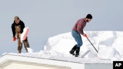 D.J. Schloss, left, and Doug Metz clear snow from a roof on Abbey Lane in Alden, N.Y., Nov. 20, 2014.