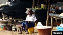 A girl sells food at a market in Beyla, Guinea, June 4, 2014. In a southeastern corner of Guinea, the Simandou mountain range rises above the forest. Under its slopes lies iron ore, a treasure long coveted by the world's miners. 