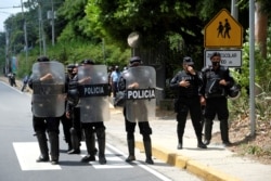 FILE - Nicaraguan police officers block journalists working outside the house of opposition leader Cristiana Chamorro after prosecutors sought her arrest for money laundering and other crimes, in Managua, June 2, 2021.