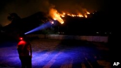 A youth wearing a head lamp watches a forest fire rage on a mountain in Cajon del Maipo, on the outskirts of Santiago, Chile, Jan. 24, 2017. Chile is suffering one of the worst wildfires in its history.