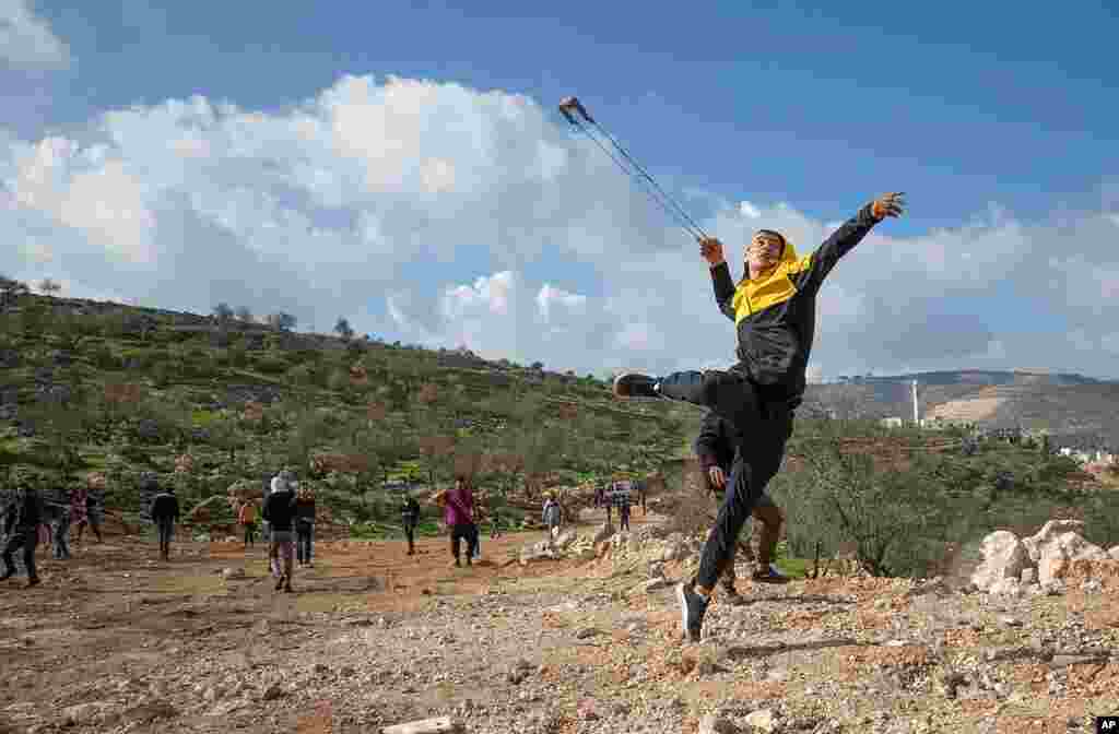 Palestinian protesters use slingshots against Israeli soldiers during clashes, at the outskirts of the West Bank village of Mughayer, north of Ramallah.