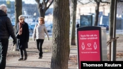 People strollIing in the cold but sunny weather pass a sign asking to maintain social distancing, amid the continuous spread of the coronavirus disease (COVID-19) pandemic, in Stockholm, Sweden.