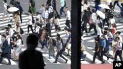 Seorang pria duduk di dekat jendela saat orang-orang yang memakai masker berjalan di sepanjang penyeberangan pejalan kaki di distrik Shibuya, 30 September 2021, di Tokyo. (Foto: AP)