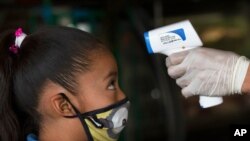 A health worker takes a child's temperature to help curb the spread of the new coronavirus, at the Central de Abasto market in Mexico City, June 18, 2020. 