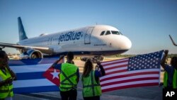 Pekerja di Bandara Internasional Jose Marti di Havana, Kuba, mengibarkan bendera AS dan Kuba menyambut penerbangan perdana maskapai Jet Blue dari Boston, AS, pada 10 November 2018. (Foto: AP/Desmond Boylan)