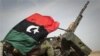 A Libyan rebel is covered up in the rebels flag next to his weapon as he moves on the road bewteen Al-Egila and Ras Lanuf, eastern Libya, Sunday, March 27, 2011