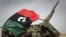 A Libyan rebel is covered up in the rebels flag next to his weapon as he moves on the road bewteen Al-Egila and Ras Lanuf, eastern Libya, Sunday, March 27, 2011