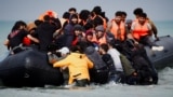 Migrants attempting to cross the English Channel to reach Britain get on an inflatable dinghy as the French police and gendarmes officers patrol on the beach of the Slack dunes in Wimereux, France.