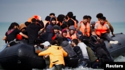 Migrants attempting to cross the English Channel to reach Britain get on an inflatable dinghy as the French police and gendarmes officers patrol on the beach of the Slack dunes in Wimereux, France. REUTERS/Benoit Tessier