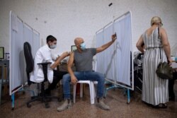 FILE - An Israeli man takes a selfie while receiving the third Pfizer-BioNTech COVID-19 vaccine from medical staff at a coronavirus vaccination center in Ramat Gan, Israel, Aug. 30, 2021.