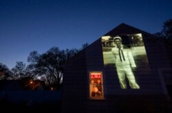 An image of veteran James Mandeville is projected onto the home of his daughter, Laurie Mandeville Beaudette, as she looks out a window with her son, Kyle, left, and husband, Mike, in Springfield, Mass., May 12, 2020.