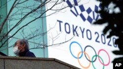Un hombre que usa una máscara protectora para ayudar a frenar la propagación del coronavirus camina cerca de la pancarta de los Juegos Olímpicos de Tokio 2020, el jueves 25 de febrero de 2021 en Tokio.