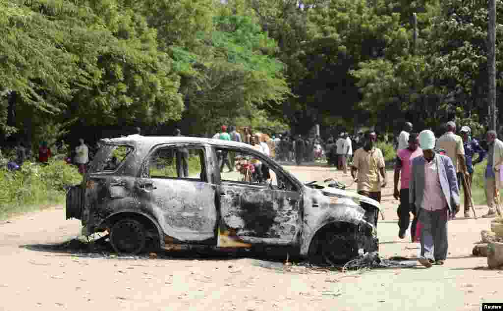 People walk past the wreckage of a car destroyed when gunmen attacked the coastal Kenyan town of Mpeketoni, June 18, 2014. 