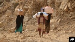 FILE - Yemenis carry relief supplies as they walk along a path outside the city of Taiz, Yemen, Jan. 17, 2016.