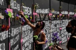 Mujeres colocan flores en una cerca perimetral instalada frente al Palacio Nacional horas antes de la manifestación por el Día Internacional de la Mujer, en la Ciudad de México, el domingo 7 de marzo de 2021.
