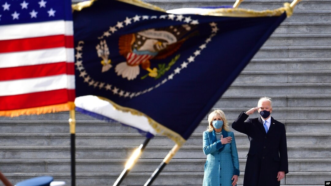 President Joe Biden salutes as his wife, Jill, puts her hand over her heart as they review the troops from the steps of the US Capitol during the inauguration, Jan. 20, 2021, in Washington. 