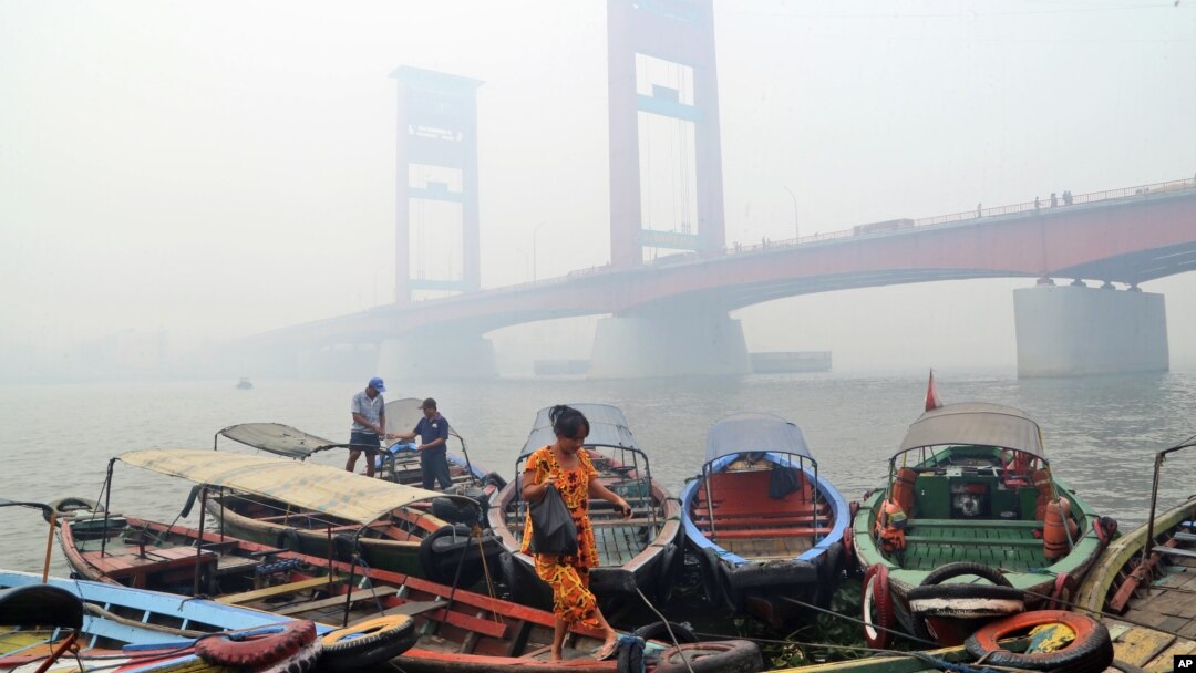 FILE - A woman disembarks from a boat as the Ampera Bridge is shrouded in haze from wildfires in Palembang, South Sumatra, Indonesia.