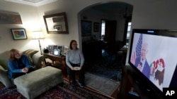 FILE - Lally Doerrer, right, and Katharine Hildebrand watch Joe Biden during his Illinois virtual town hall, in Doerrer's living room in Chicago, March 13, 2020.