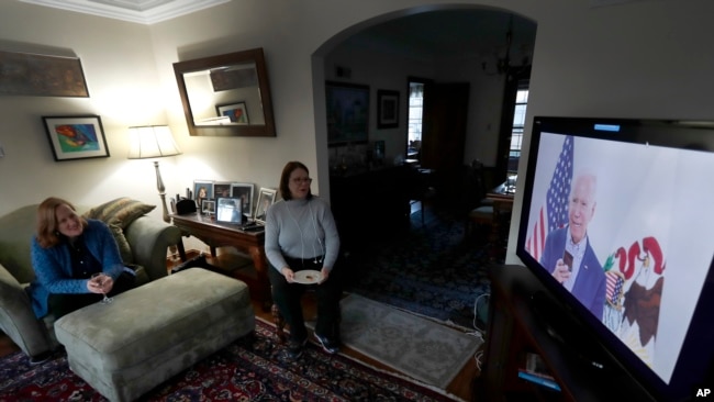 Lally Doerrer, right, and Katharine Hildebrand watch Joe Biden during his Illinois virtual town hall, in Doerrer's living room Friday, March 13, 2020, in Chicago. (AP Photo/Charles Rex Arbogast)