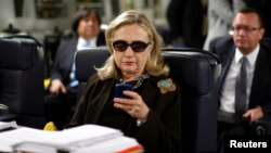 FILE - Then U.S. secretary of state Hillary Clinton checks her mobile phone upon her departure in a military C-17 plane from Malta bound for Tripoli, Libya, Oct. 18, 2011.