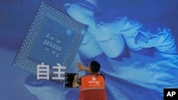 FILE - A worker checks the display panel showing a computer chip and the Chinese words for "independence" at a booth during the World AI Conference in Shanghai on July 5, 2023. Artificial intelligence competition between China and the United States is at a possible turning point.