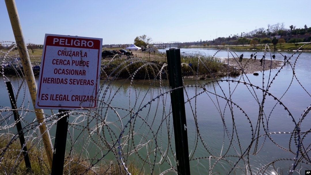 Migrantes cruzan el río Bravo a EEUU desde México detrás de un hilo de cuchillas y un cartel que advierte que cruzar es peligroso e ilegal, el miércoles 3 de enero de 2024 en Eagle Pass, Texas. 