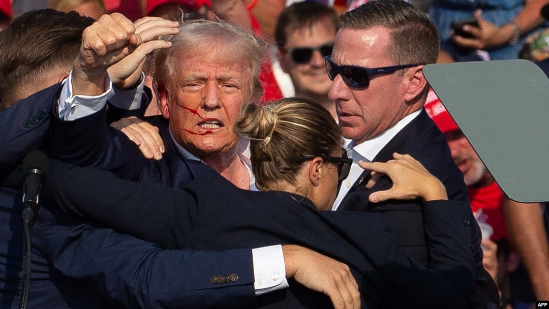 Ứng cử viên Đảng Cộng hòa Hoa Kỳ Donald Trump với vết máu trên khuôn mặt, được bao quanh bởi các mật vụ, khi ông được đưa ra khỏi sân khấu tại một cuộc vận động ở Butler, bang Pennsylvania, vào ngày 13/7/2024.