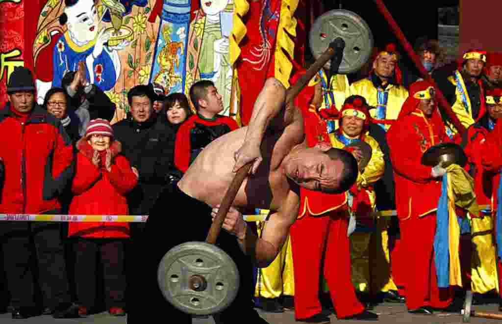 Sebuah pertunjukkan oleh penampil yang dikenal sebagai "orang kuat" mengangkat beban di satu bahu di depan para penonton di kuil Dongyue, Beijing, 23 Januari (Reuters).