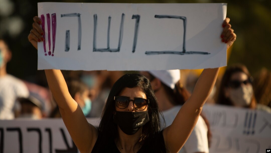 An Israeli social worker holds a sign in Hebrew that reads, "shame," during a protest against the economic situation in the central Israeli town of Kfar Ahim, July 9, 2020.