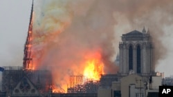 Flames rise from Notre Dame cathedral as it burns in Paris, Monday, April 15, 2019. Massive plumes of yellow brown smoke is filling the air above Notre Dame Cathedral and ash is falling on tourists and others around the island that marks the center of Par