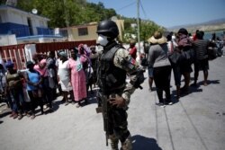 A Haitian National Police (PNH) officer looks on as Haitians stand behind him in the in the border of Malpasse, Haiti, March 17, 2020.