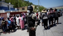 A Haitian National Police (PNH) officer looks on as Haitians stand behind him in the in the border of Malpasse, Haiti, March 17, 2020. 